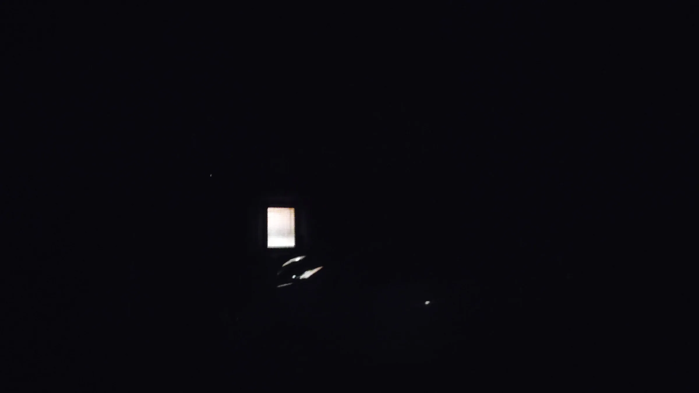 A framed picture glowing on a wall in an otherwise black room, its contents burnt out to white, with a few small highlights below it.