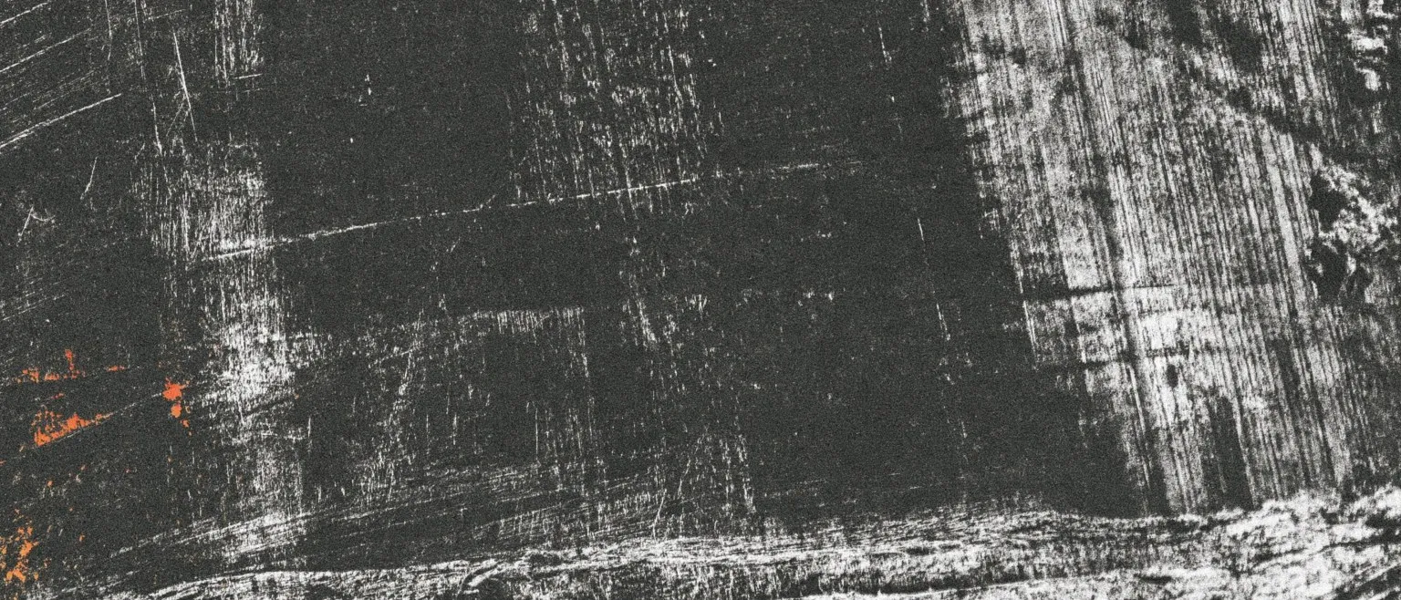 Coarse horizontal grain, silver over black, small orange flares along the lower edge.