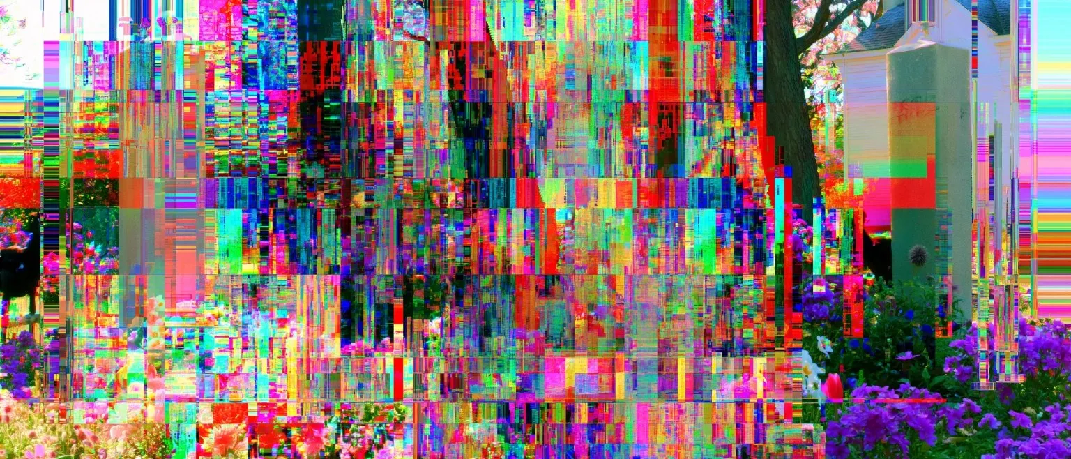 Dense multicoloured pixel-block glitch over a garden with a house and blossoming trees, purple flowers massed at the lower right.